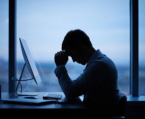 Tired or stressed businessman sitting in front of computer in office