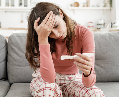 Young European woman worried because she has got positive results of pregnancy test, sitting alone at home