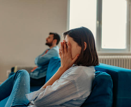 Unhappy Couple After an Argument in the Living Room at Home. Sad Pensive Young Girl Thinking of Relationships Problems Sitting on Sofa With Offended Boyfriend, Conflicts in Marriage, Upset Couple After Fight Dispute, Making Decision of Breaking Up Get Divorced